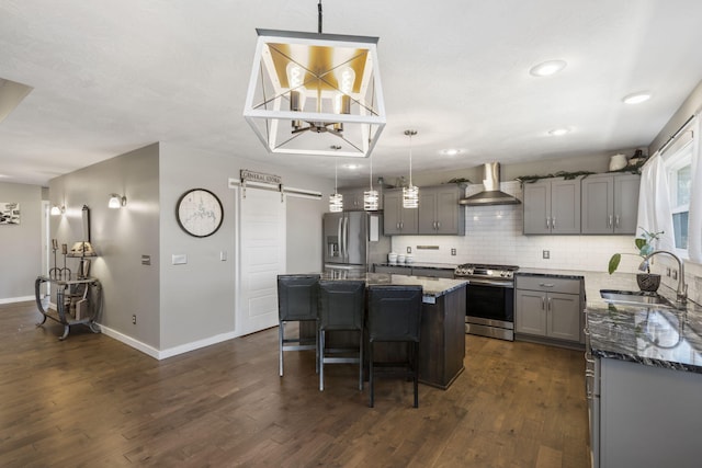 kitchen featuring a barn door, gray cabinets, stainless steel appliances, wall chimney range hood, and a sink