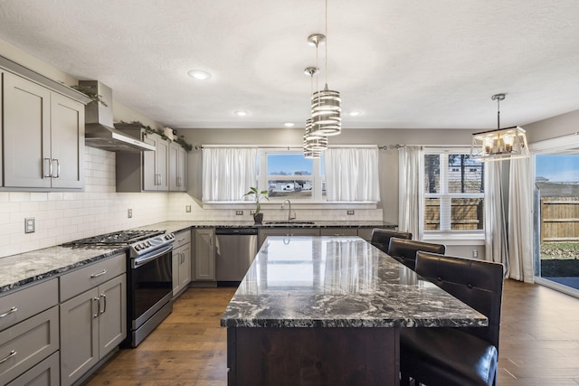 kitchen with stainless steel appliances, a kitchen bar, backsplash, gray cabinetry, and wall chimney exhaust hood