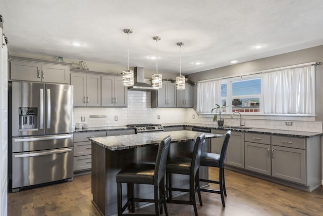 kitchen featuring gray cabinetry, dark wood-style flooring, appliances with stainless steel finishes, wall chimney range hood, and a center island