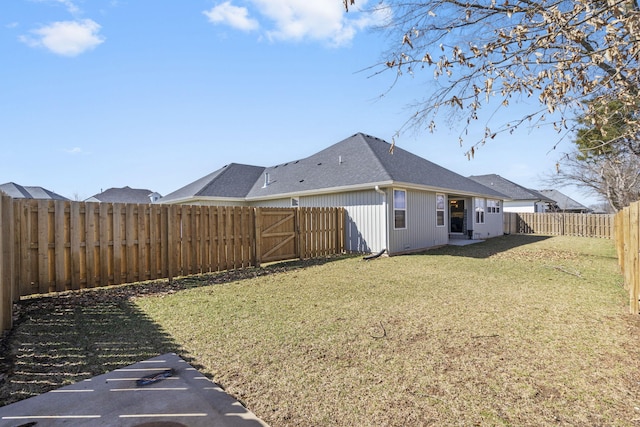 back of property with a shingled roof, a fenced backyard, and a yard