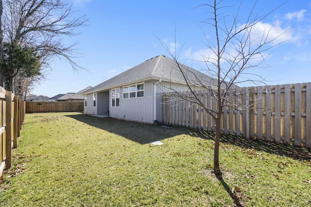 rear view of property with roof with shingles, a lawn, and a fenced backyard