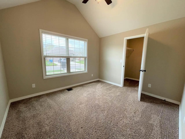 carpeted empty room featuring lofted ceiling, baseboards, visible vents, and a ceiling fan