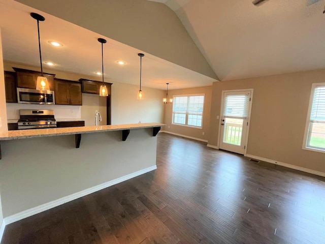 kitchen with light stone counters, dark wood-style flooring, baseboards, appliances with stainless steel finishes, and a kitchen bar