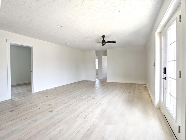 spare room featuring a textured ceiling, ceiling fan, light wood-type flooring, and baseboards