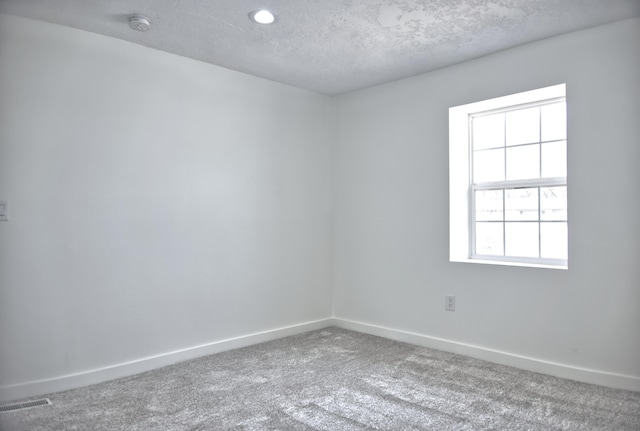 unfurnished room with a textured ceiling, carpet, visible vents, and baseboards