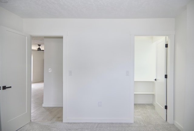 unfurnished bedroom with a spacious closet, a textured ceiling, baseboards, and carpet flooring