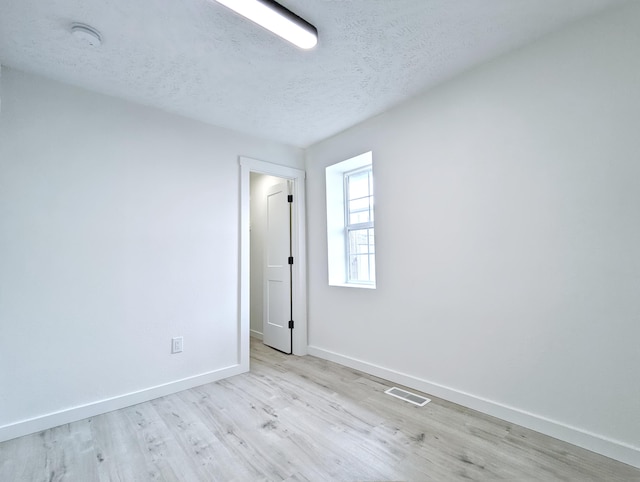 spare room featuring visible vents, a textured ceiling, baseboards, and wood finished floors