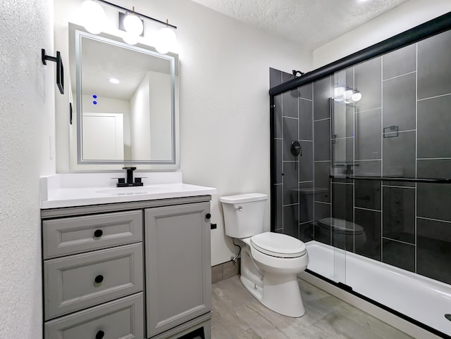 full bath featuring toilet, a stall shower, vanity, a textured ceiling, and baseboards