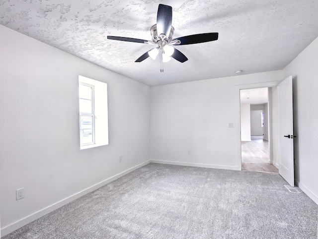 carpeted empty room featuring a ceiling fan, a textured ceiling, and baseboards