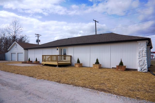 exterior space with a garage, a wooden deck, roof with shingles, and an outdoor structure