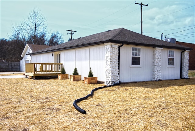 view of side of property featuring a shingled roof and a wooden deck