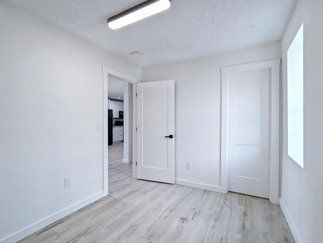 unfurnished bedroom featuring a textured ceiling, wood finished floors, freestanding refrigerator, and baseboards