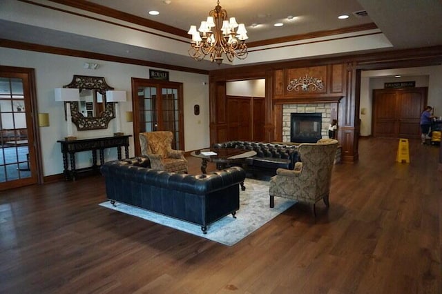 living room with a tray ceiling, dark wood-style flooring, a fireplace, ornamental molding, and a chandelier