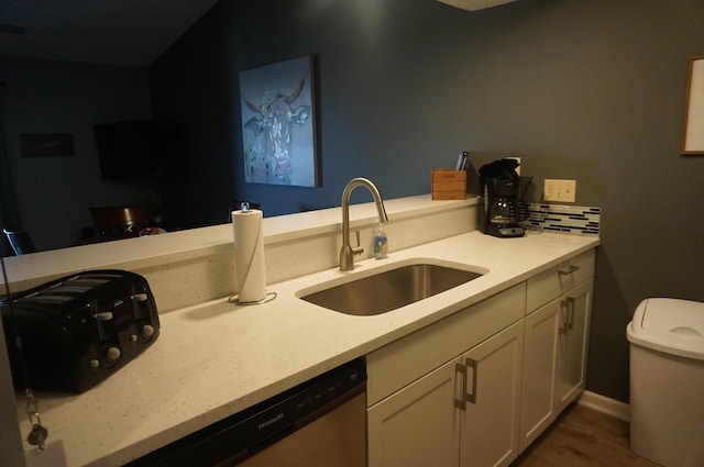 kitchen featuring wood finished floors, a sink, white cabinetry, stainless steel dishwasher, and tasteful backsplash