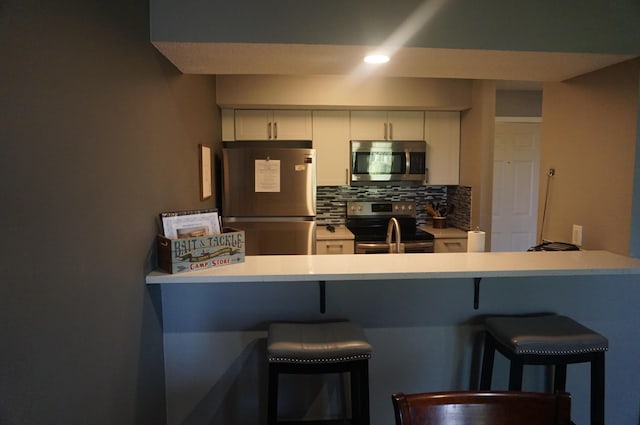 kitchen with a peninsula, appliances with stainless steel finishes, white cabinetry, and decorative backsplash