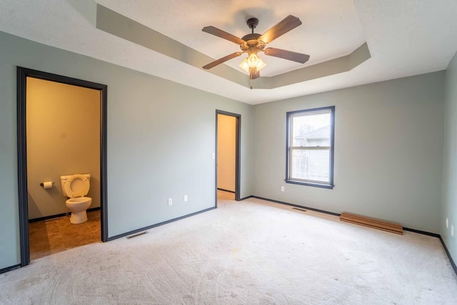 unfurnished bedroom with baseboards, visible vents, a tray ceiling, and carpet flooring