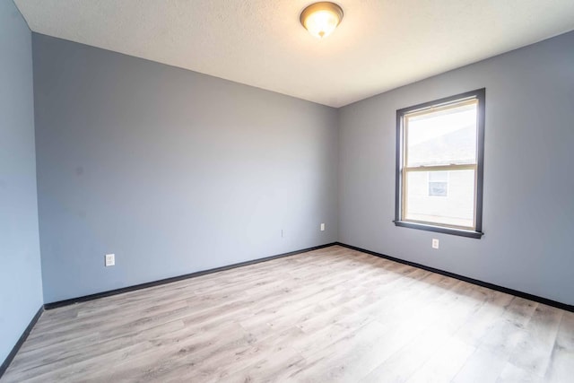 spare room with a textured ceiling, wood finished floors, and baseboards