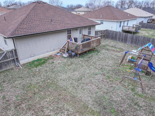 back of property featuring a wooden deck, a fenced backyard, roof with shingles, a yard, and a playground