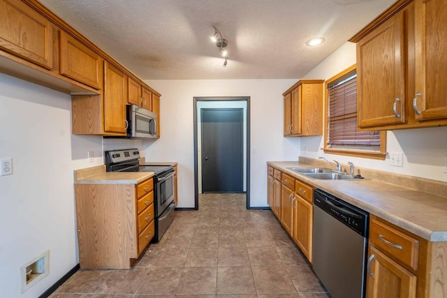 kitchen featuring a textured ceiling, appliances with stainless steel finishes, brown cabinetry, and a sink