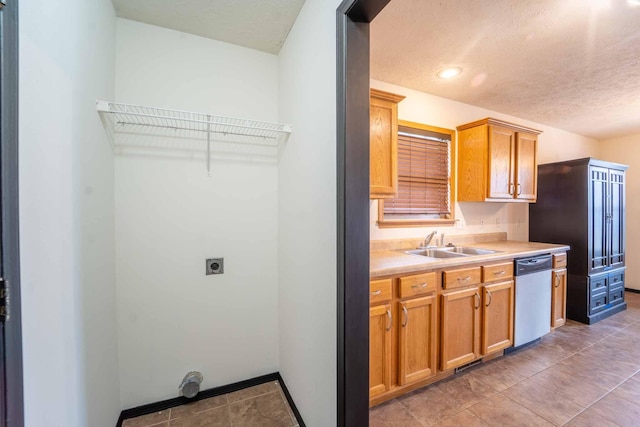 kitchen featuring light countertops, stainless steel dishwasher, a sink, a textured ceiling, and baseboards