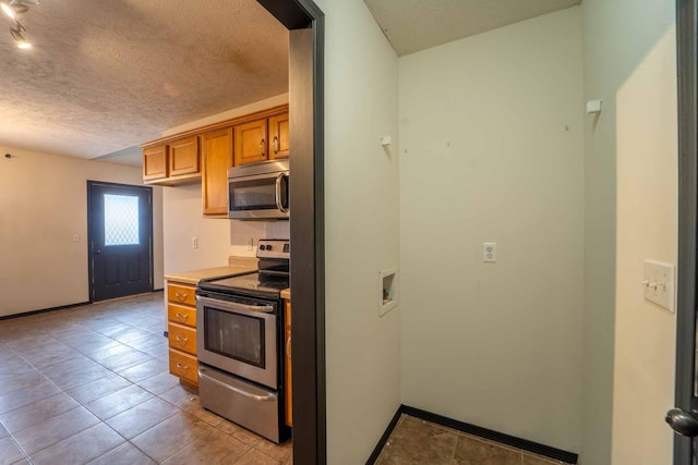 kitchen with brown cabinets, light tile patterned floors, appliances with stainless steel finishes, a textured ceiling, and baseboards