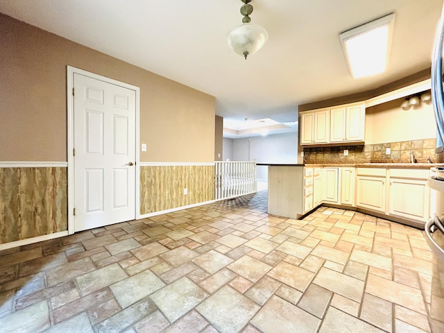 kitchen with wooden walls, wainscoting, a peninsula, cream cabinets, and stone finish flooring