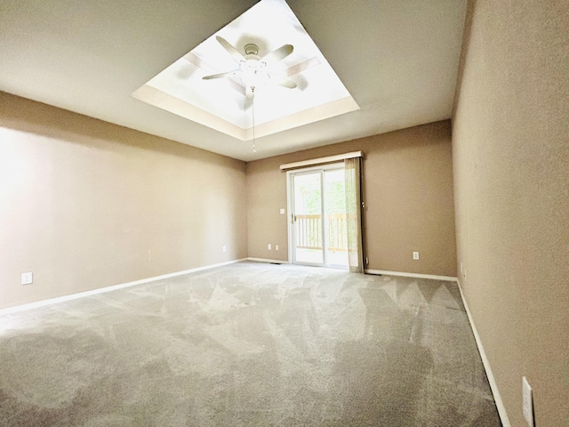 carpeted empty room with baseboards, a tray ceiling, and a ceiling fan