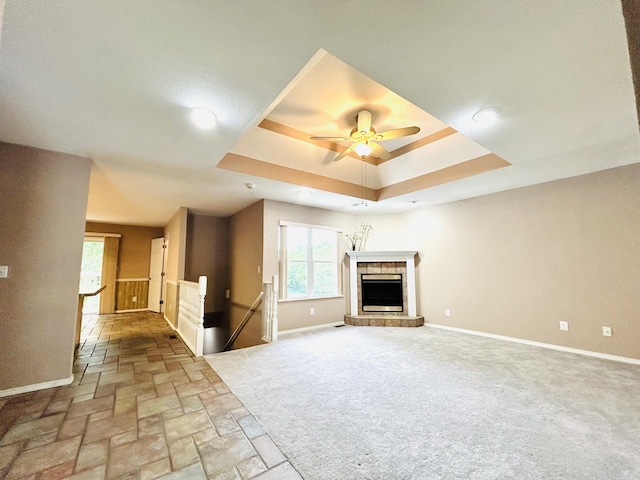 unfurnished living room with carpet, a raised ceiling, a fireplace with raised hearth, a ceiling fan, and baseboards