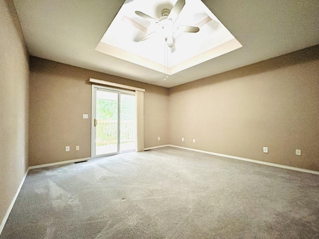 carpeted spare room with a raised ceiling, a ceiling fan, and baseboards