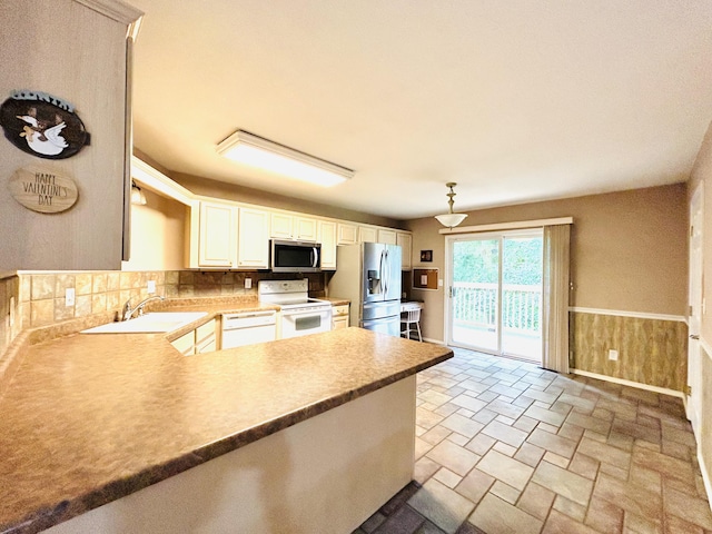 kitchen featuring wainscoting, appliances with stainless steel finishes, a peninsula, stone finish flooring, and a sink