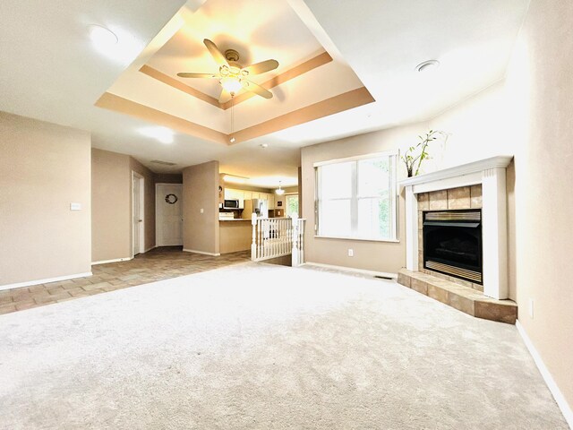 unfurnished living room featuring carpet, a raised ceiling, a tiled fireplace, and baseboards