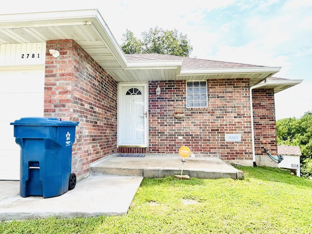 doorway to property with an attached garage, a shingled roof, a lawn, and brick siding