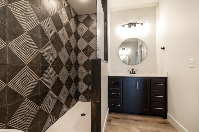 bathroom with baseboards, a tile shower, wood finished floors, and vanity