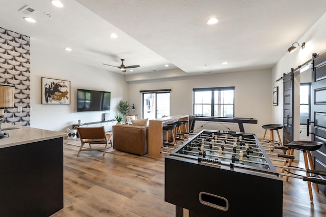 rec room featuring a barn door, ceiling fan, wood finished floors, a textured ceiling, and recessed lighting