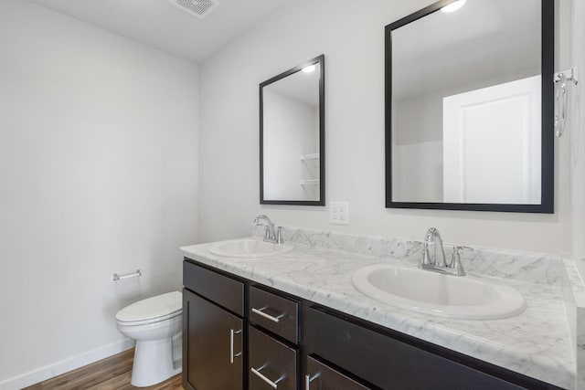 bathroom with toilet, double vanity, a sink, and visible vents