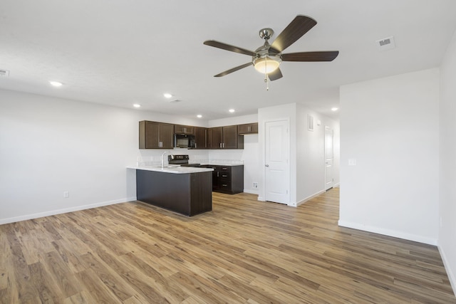 kitchen with visible vents, dark brown cabinets, light wood-type flooring, black microwave, and a peninsula