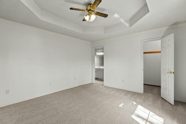 unfurnished bedroom with light carpet, baseboards, ornamental molding, a walk in closet, and a raised ceiling