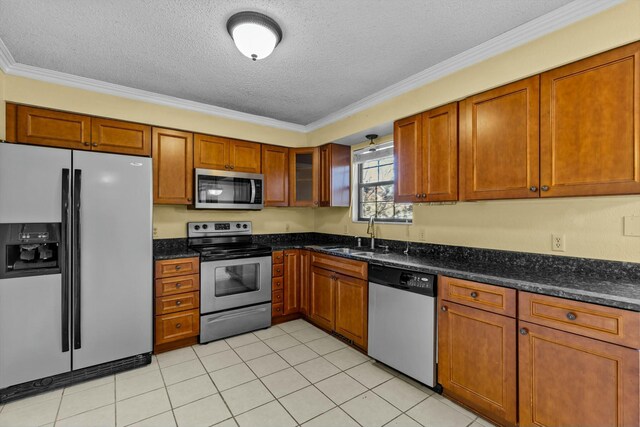 kitchen with a textured ceiling, stainless steel appliances, a sink, ornamental molding, and brown cabinets