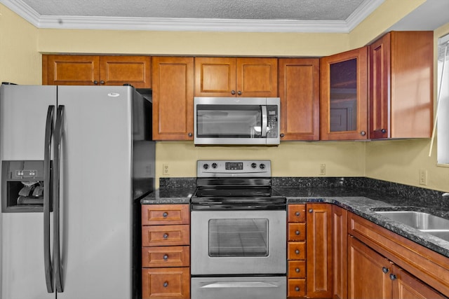 kitchen with brown cabinets, appliances with stainless steel finishes, ornamental molding, glass insert cabinets, and a sink