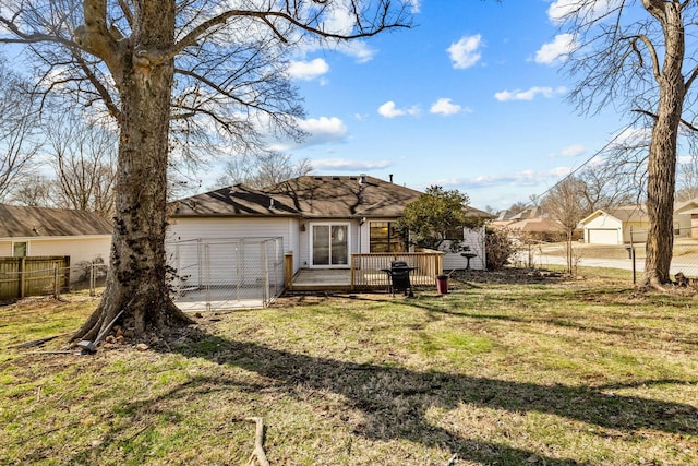 back of property featuring a garage, fence, a deck, and a lawn