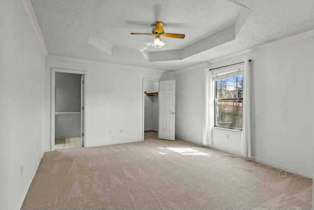 unfurnished bedroom featuring ceiling fan, ornamental molding, a tray ceiling, a textured ceiling, and carpet floors