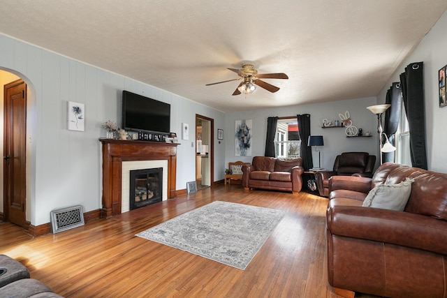 living room featuring arched walkways, a fireplace, wood finished floors, visible vents, and a ceiling fan