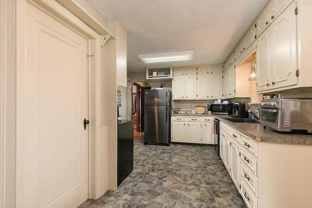 kitchen featuring a toaster, freestanding refrigerator, stone finish flooring, white cabinetry, and a sink