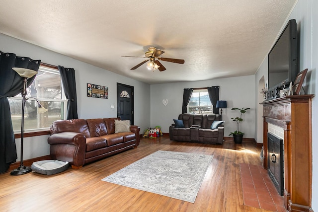 living room with a fireplace, a ceiling fan, a textured ceiling, wood finished floors, and baseboards