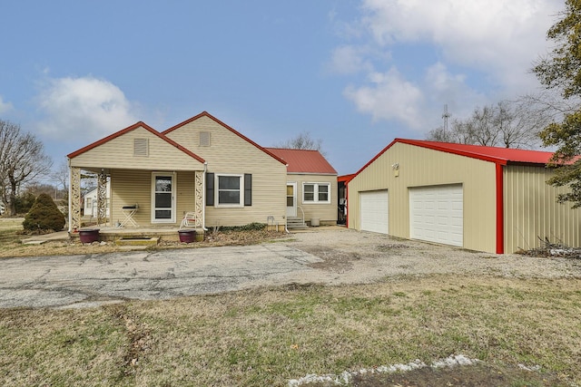 view of front facade with an outbuilding, metal roof, covered porch, a garage, and driveway