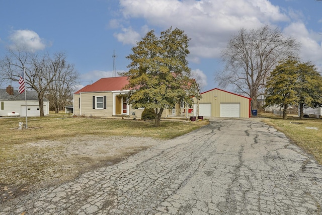 view of front facade with an outdoor structure, aphalt driveway, metal roof, and a front yard