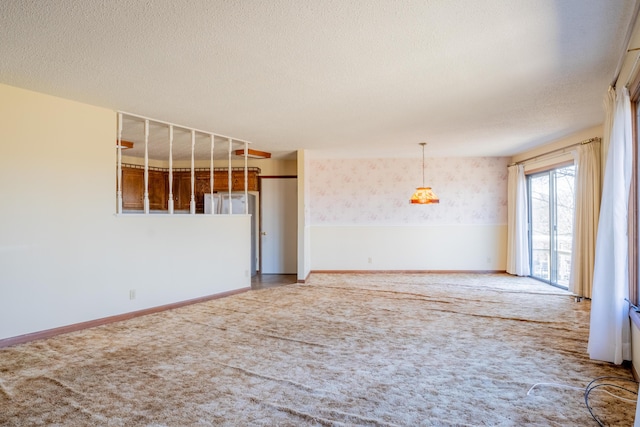 carpeted spare room featuring a textured ceiling, baseboards, and wallpapered walls