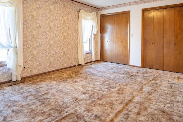 unfurnished bedroom with carpet, baseboards, and two closets