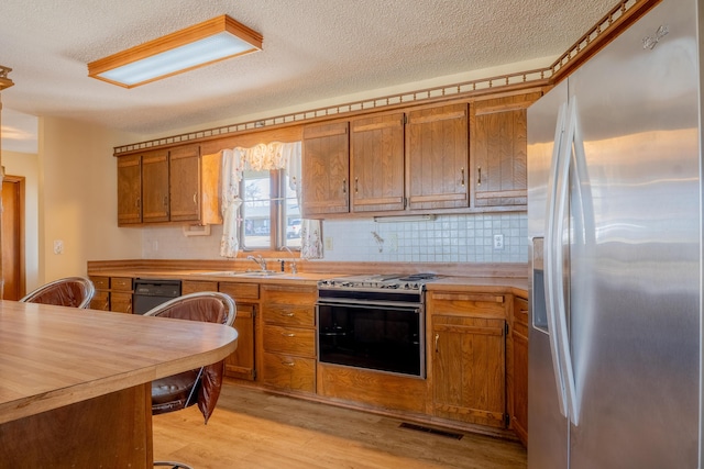 kitchen featuring brown cabinets, gas range oven, visible vents, light wood-type flooring, and stainless steel fridge with ice dispenser