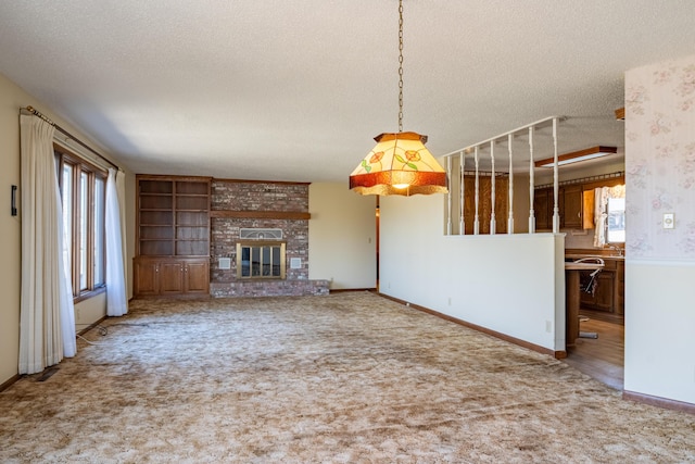 unfurnished living room with carpet floors, a brick fireplace, a textured ceiling, and baseboards